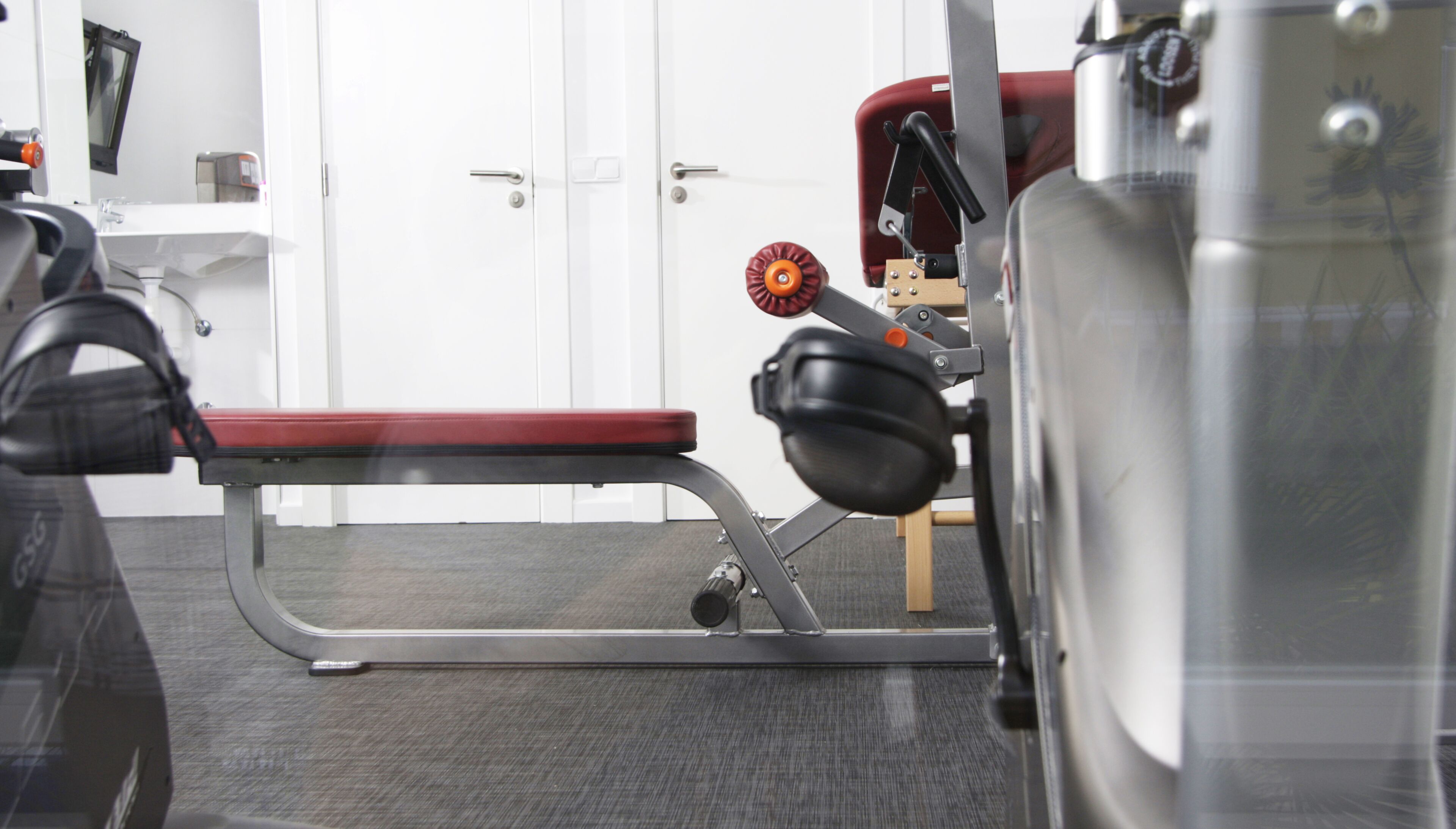 Un gimnasio con equipo de ejercicio, una banca y una puerta al fondo.