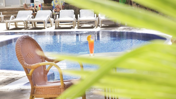 Un espace piscine avec des chaises longues et une table où l'on peut prendre une boisson.