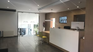Un espace d’accueil avec un comptoir de réception blanc, un écran d’ordinateur et un extincteur fixé au mur.