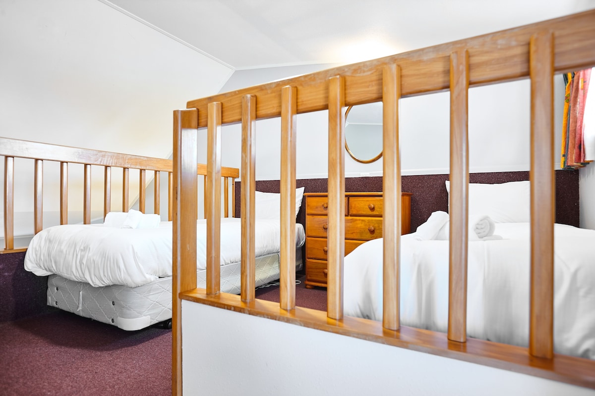 A room with two beds, a wooden headboard, a dresser, and a mirror.