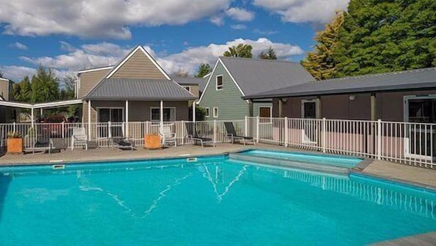 A swimming pool with lounge chairs and a fenced deck area, surrounded by buildings with a simple architectural style. - Turangi Leisure Lodge (Turangi)