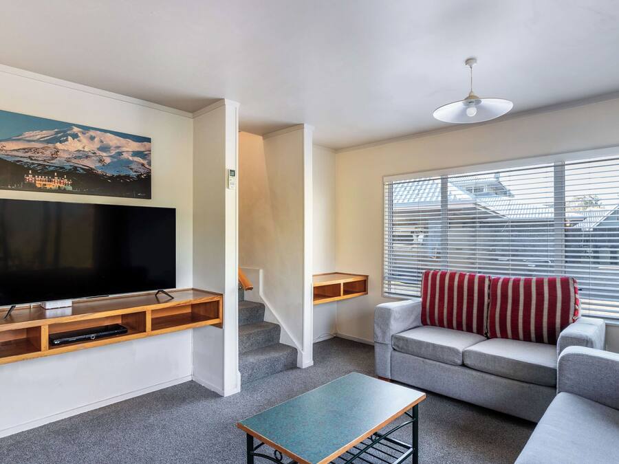 A living room with a flat-screen TV, a sofa, a coffee table, and a window with blinds.