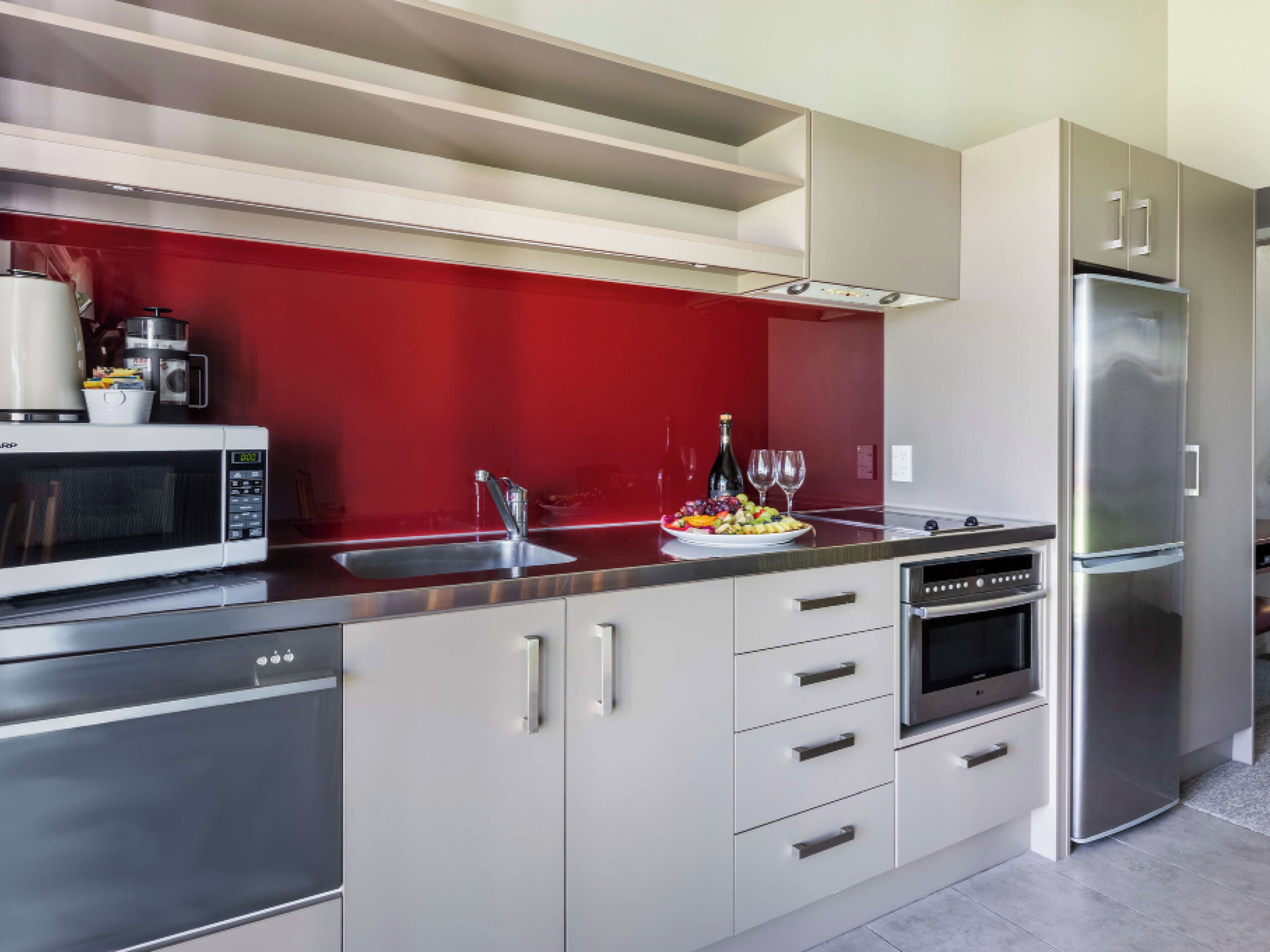Una cocina moderna con electrodomésticos de acero inoxidable, un salpicadero rojo y una bandeja de fruta en la encimera.