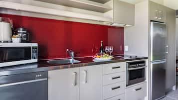 Una cocina moderna con electrodomésticos de acero inoxidable, un salpicadero rojo y una bandeja de fruta en la encimera.