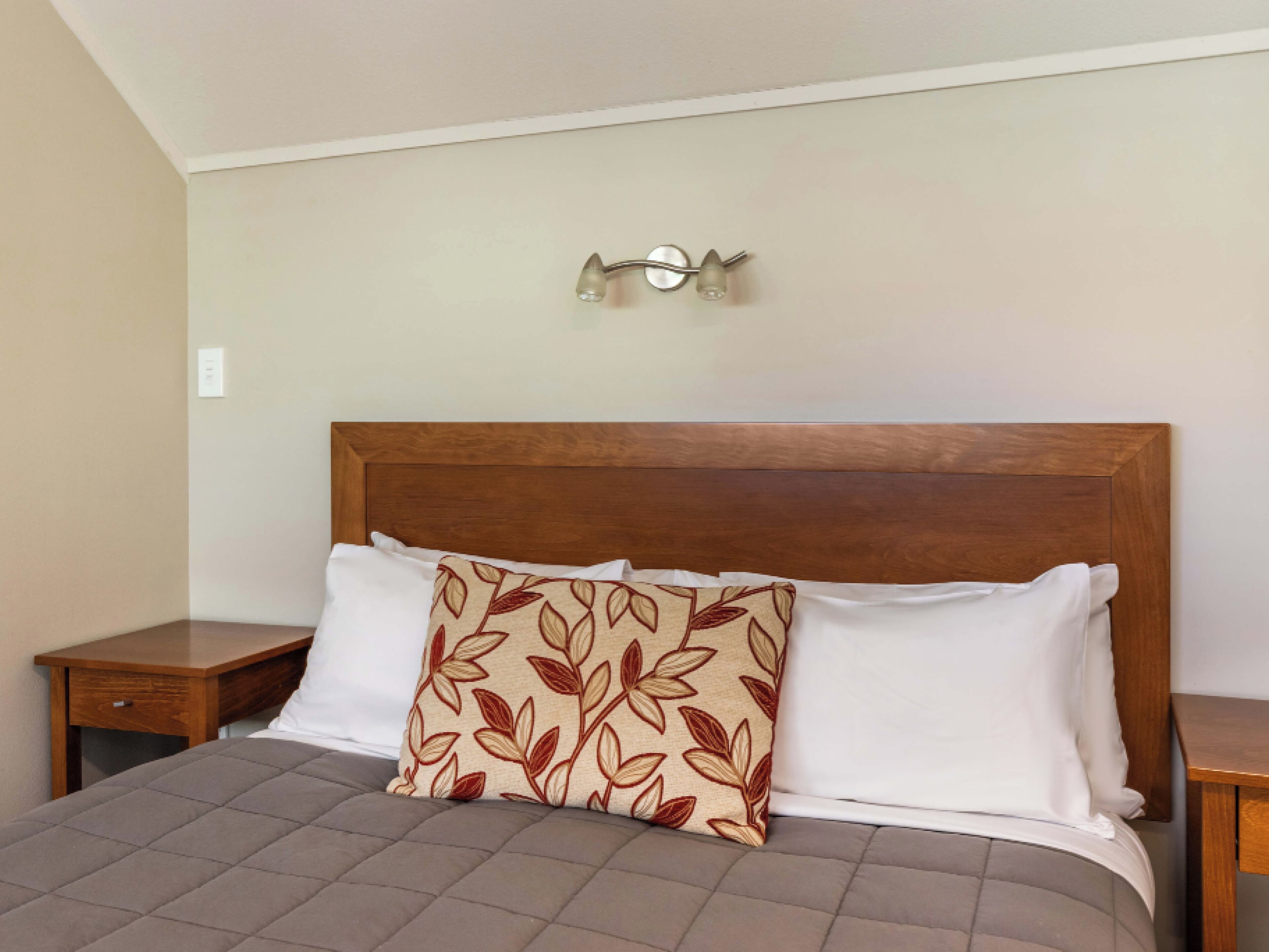 A neatly made bed with a wooden headboard, a decorative pillow, and a bedside table.