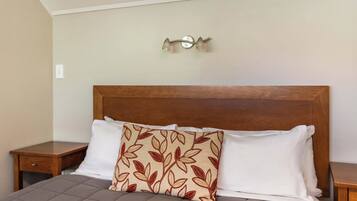 A neatly made bed with a wooden headboard, a decorative pillow, and a bedside table.