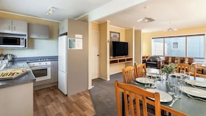 A compact kitchen with modern appliances, a dining area with wooden chairs, and a television in the living space. - Turangi Leisure Lodge (Turangi)