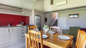 A modern kitchen with a red backsplash, stainless steel appliances, and a dining area with wooden furniture and a staircase leading to another level.