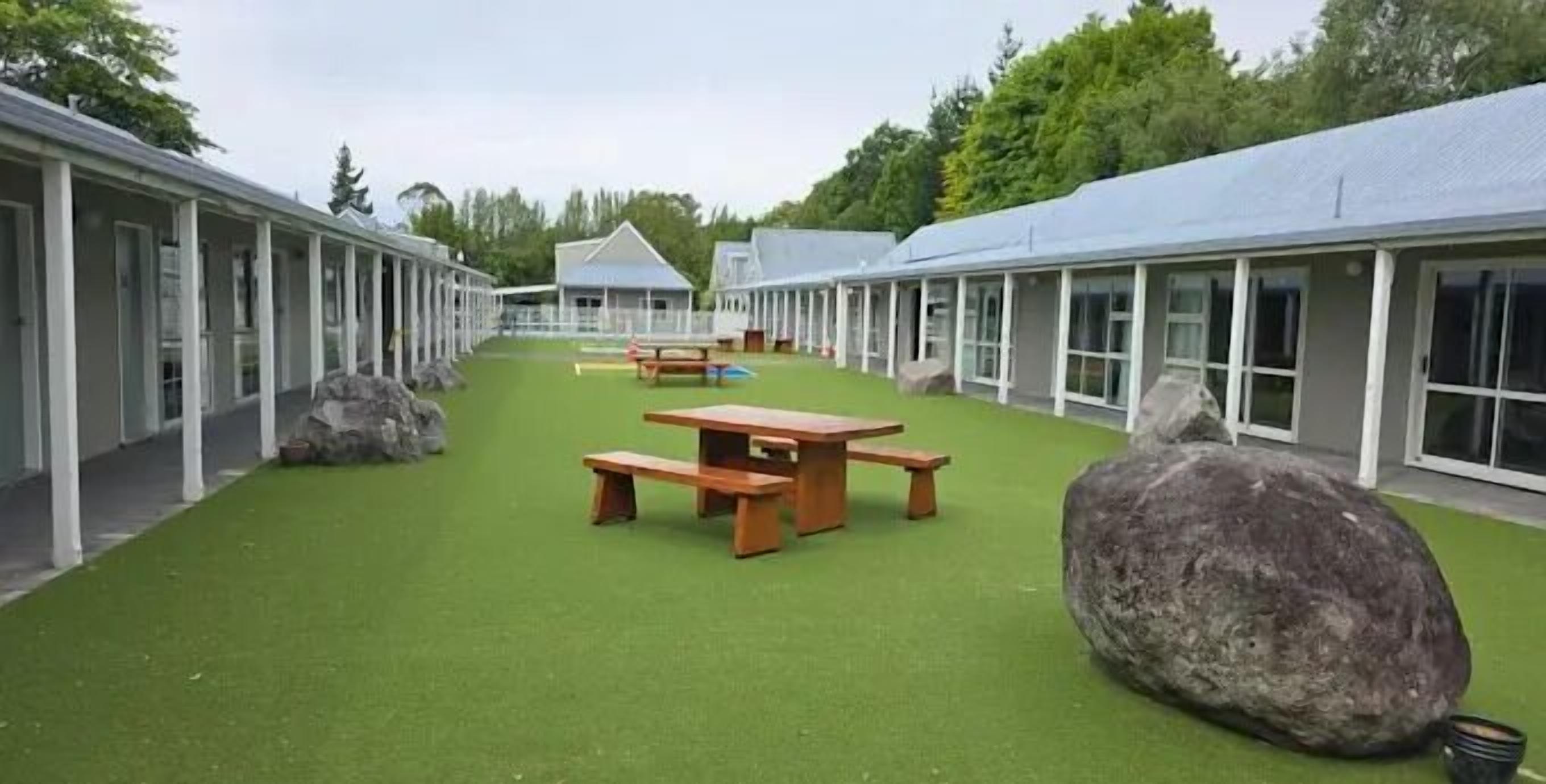 A courtyard with a picnic table and benches, surrounded by buildings with large windows and a grassy area.