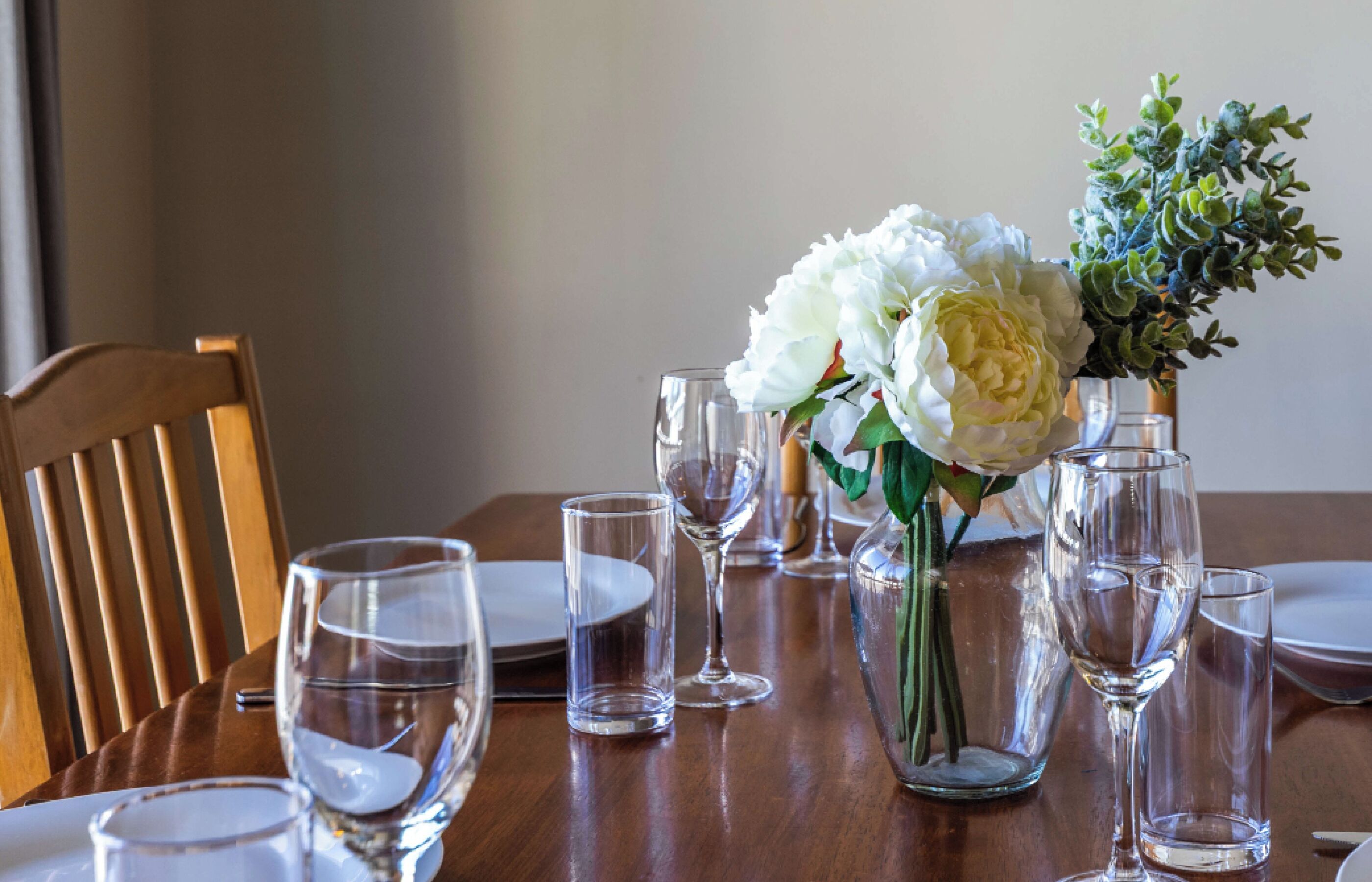 A dining table set with clear glassware and a vase with white flowers.