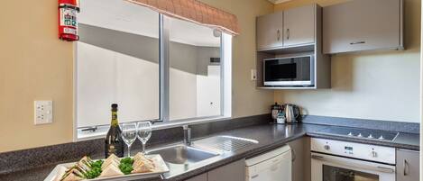 A modern kitchen with a granite countertop, stainless steel appliances, and a large window with blinds.