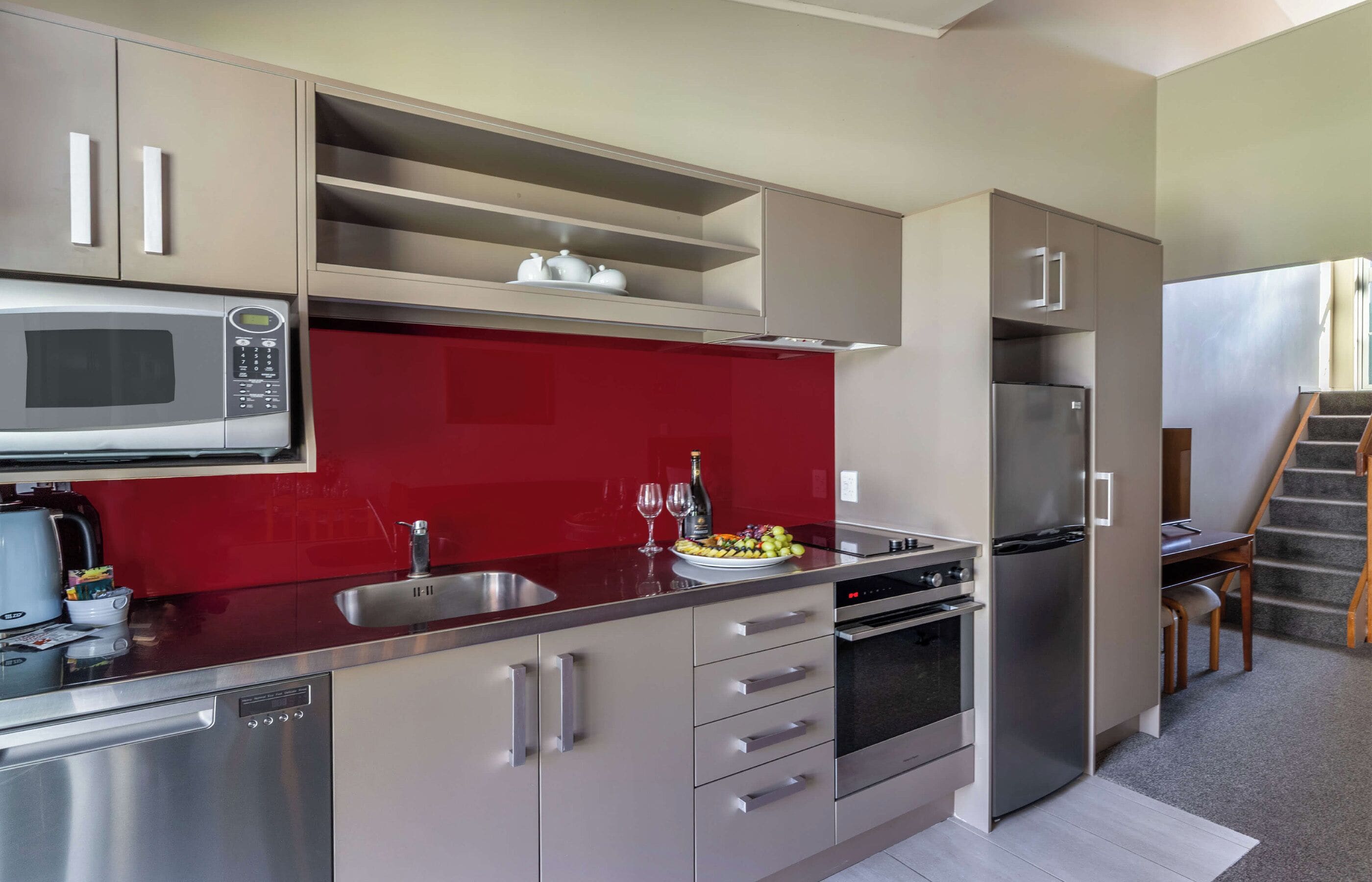 A modern kitchen with stainless steel appliances, a red backsplash, and a built-in oven.