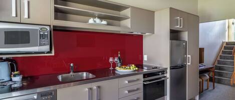 A modern kitchen with stainless steel appliances, a red backsplash, and a built-in oven.