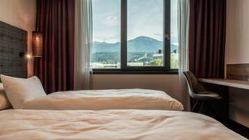 A hotel room with two beds, a desk, and a view of mountains through a window.