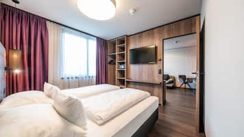 Habitación de hotel con dos camas, televisión, armario de madera y zona de estar con una silla y una mesa.