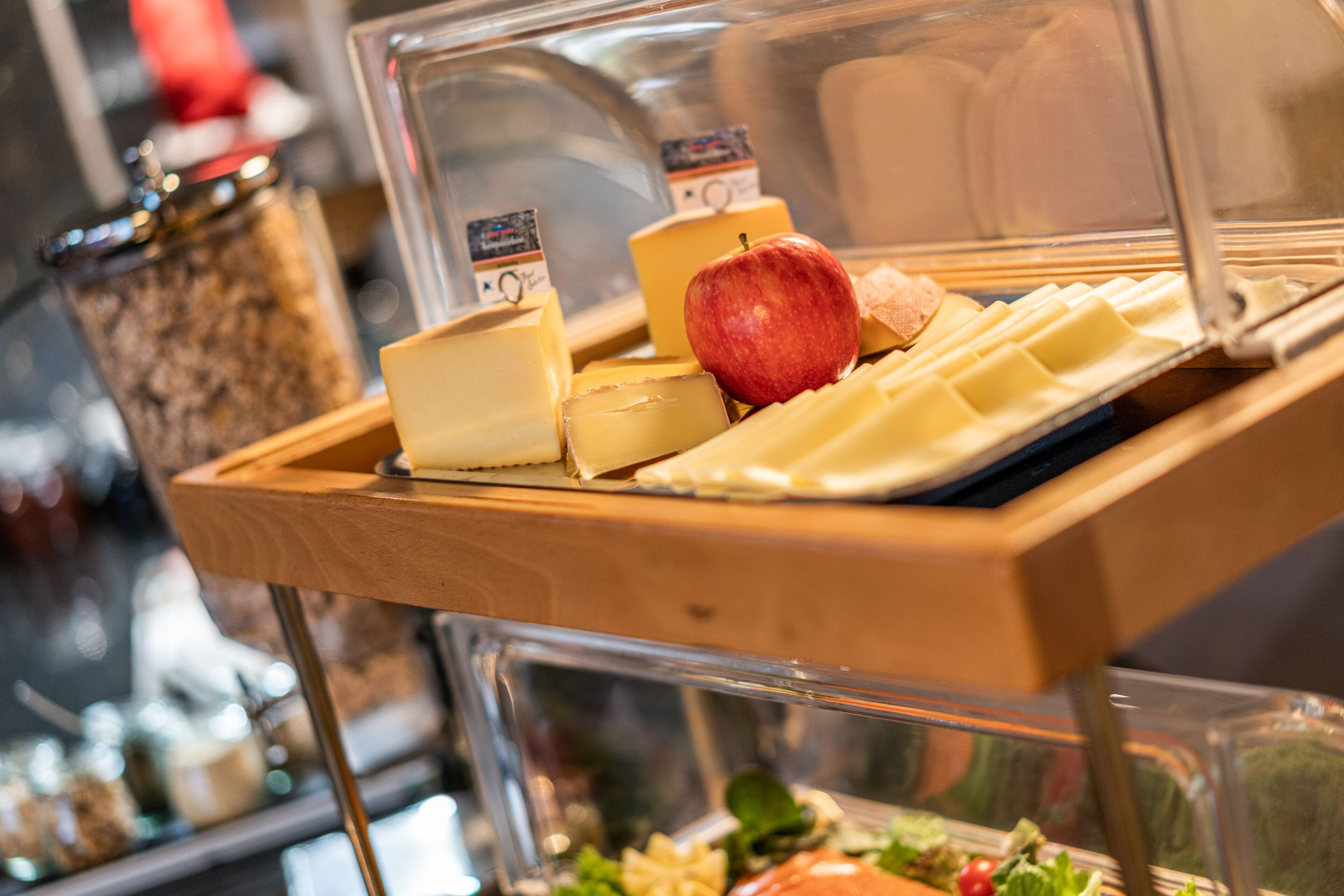 A cheese and fruit display with a wooden tray and a glass case.
