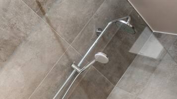 Ducha moderna con cabezal de ducha de mano y cabezal de ducha fijo montado en la pared, sobre un suelo de azulejos.