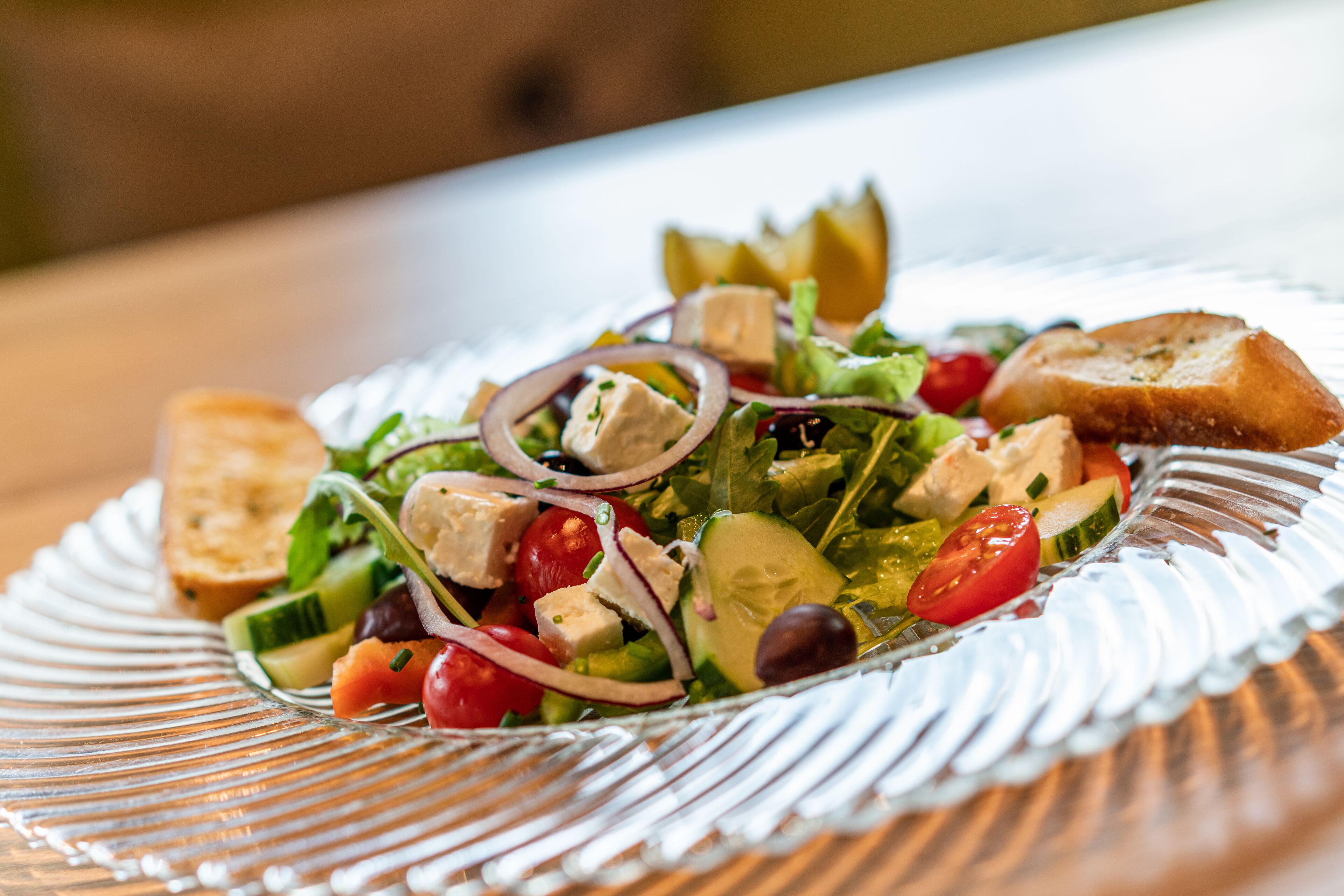 Ein Glasplatten-Teller mit Salat auf einem Holztisch.
