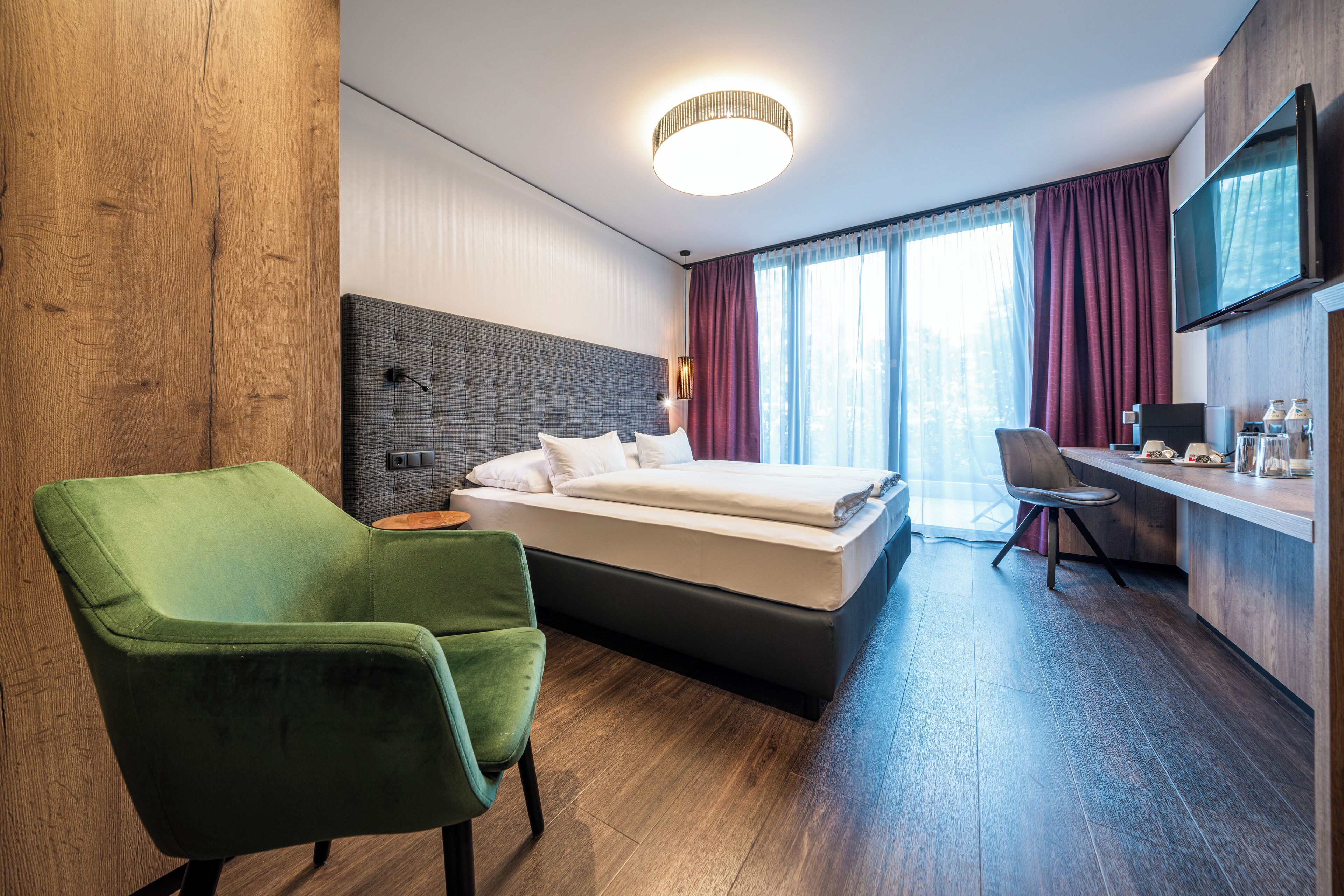 Une chambre d’hôtel moderne avec un grand lit, un fauteuil vert, un bureau et une télévision.