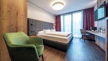 Une chambre d’hôtel moderne avec un grand lit, un fauteuil vert, un bureau et une télévision.