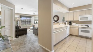 A modern kitchen with white cabinets, a microwave, and a stove. There is a dining area with a table and chairs. - Walk-in Golf Condo with Course View from All-Season Sunroom (Branson)