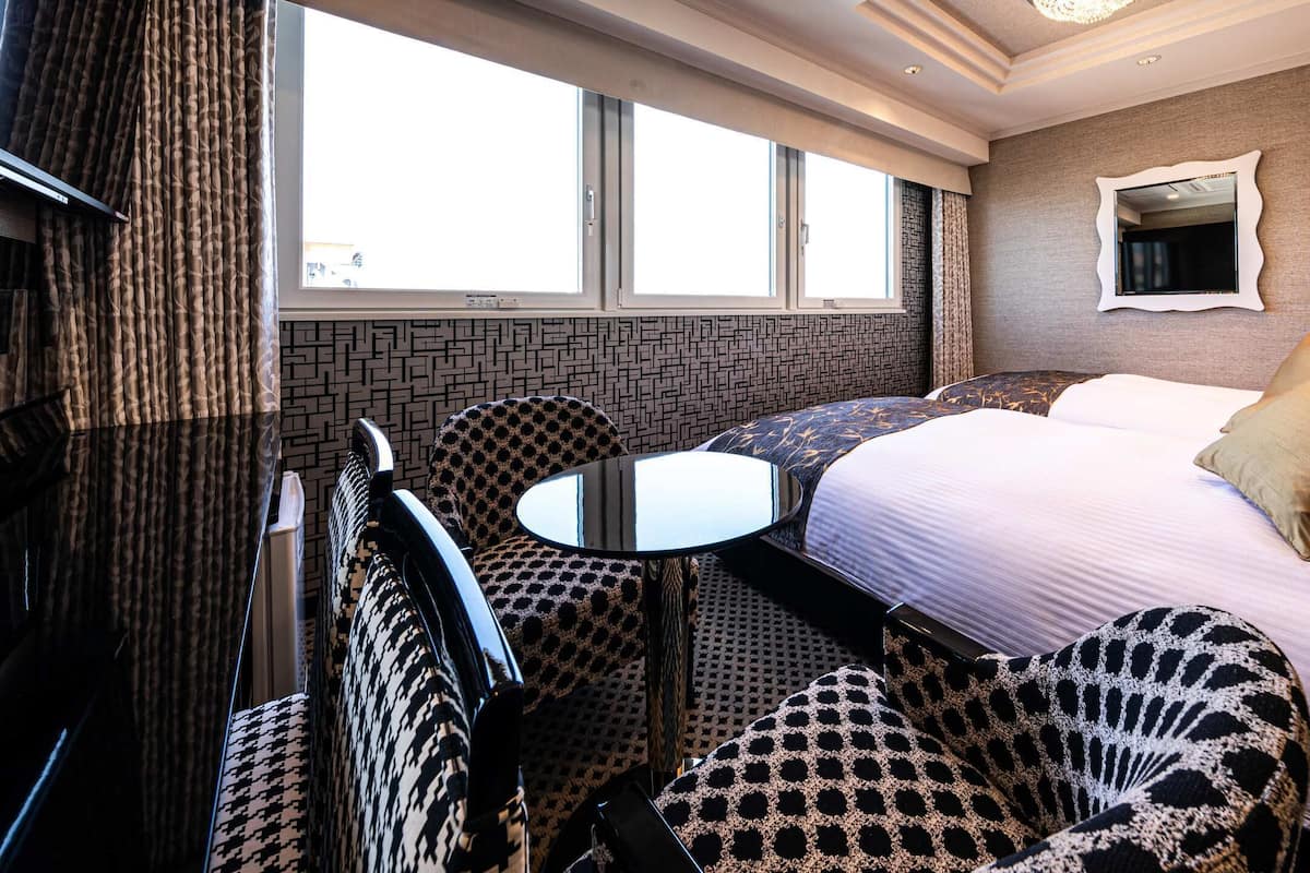 A hotel room with a bed, two armchairs, a small table, a mirror, and a window.