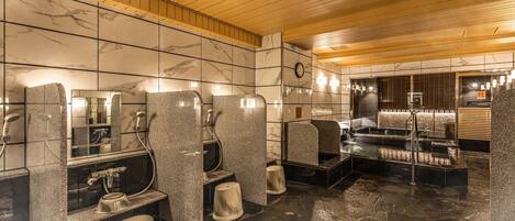 Baño público con separadores de granito, paredes de mármol y suelo de piedra.