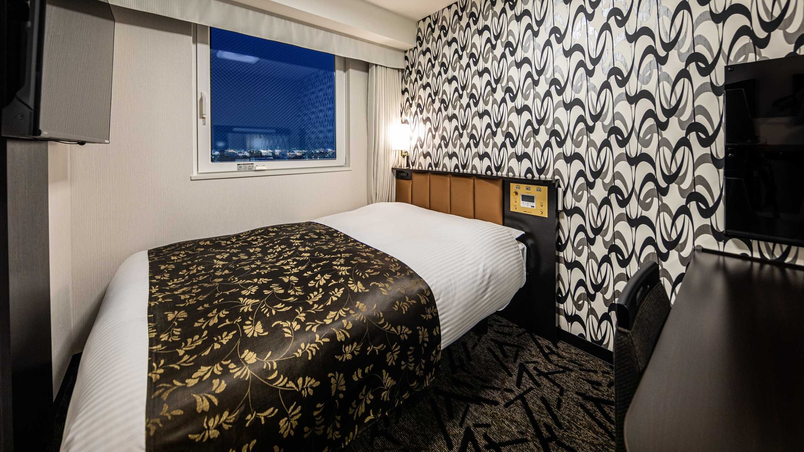Quarto de hotel com cama, janela, parede estampada e televisão.