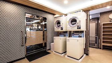 A laundry room with two washing machines and a dryer, a patterned wall, and a door with an automatic closing sign.