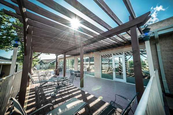 Un patio al aire libre cubierto con vigas de madera, sillas y mesas de metal.