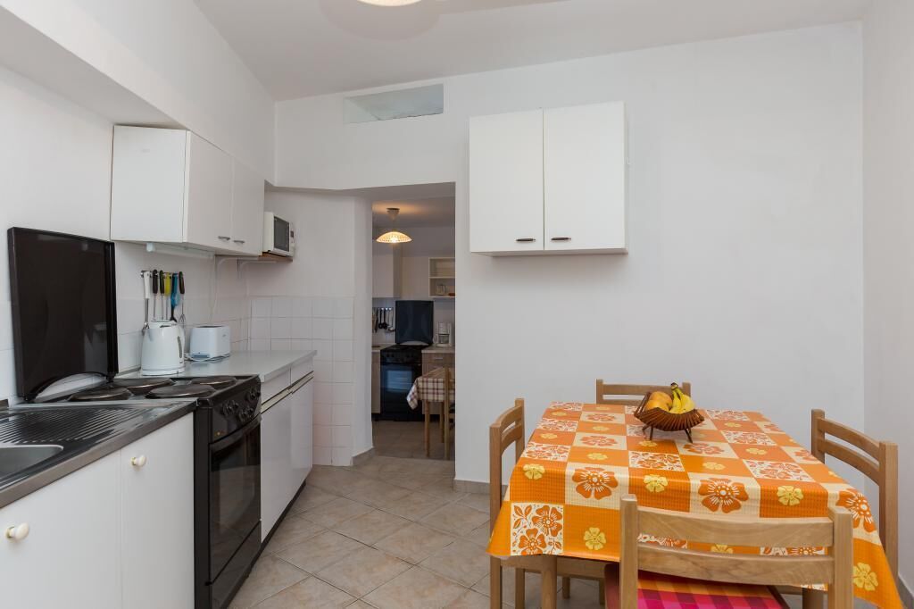 A compact kitchen with a stove, oven, and microwave. There is a dining table with a floral tablecloth and chairs.