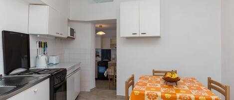A compact kitchen with a stove, oven, and microwave. There is a dining table with a floral tablecloth and chairs.