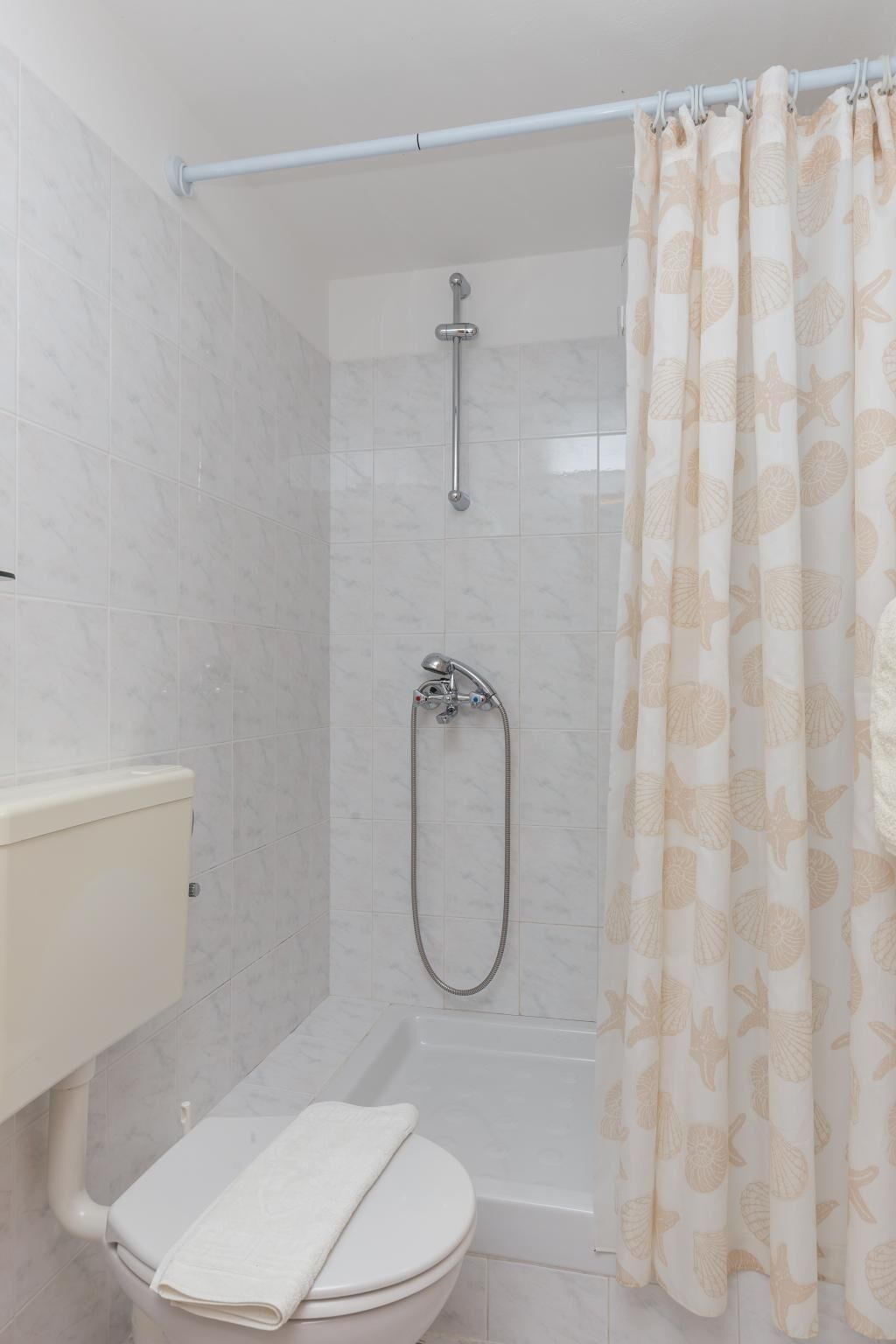A bathroom with a shower, toilet, and a towel on the seat.