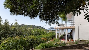 Um edifício moderno com fachada branca, cercado por vegetação exuberante e vista para colinas distantes.