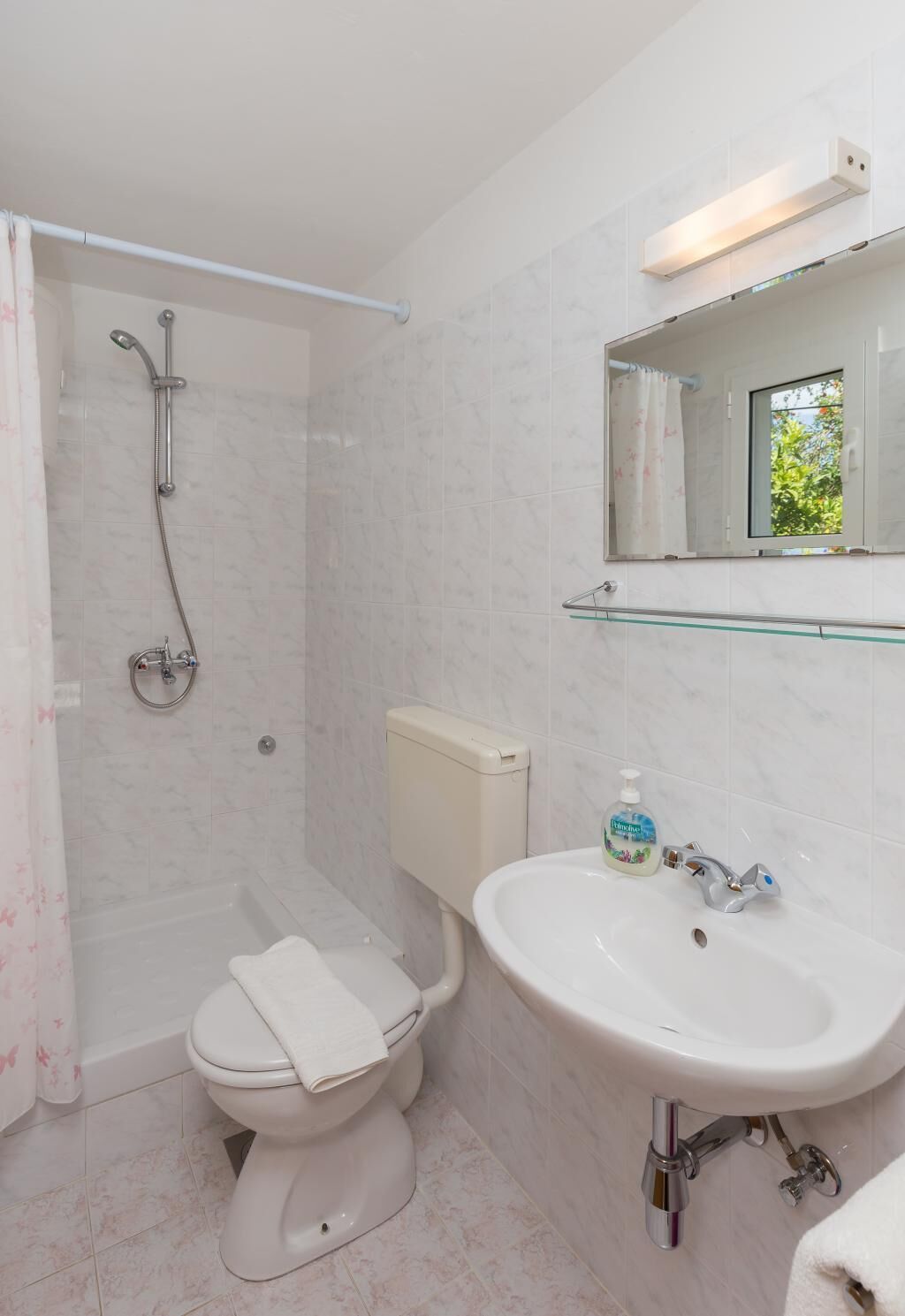A bathroom with a toilet, shower, sink, and a mirror.