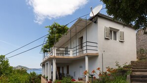 Uma casa de dois andares com varanda, antena parabólica e vista para o mar.