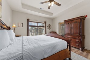 A bedroom with a bed, a wooden dresser, a ceiling fan, a window with blinds, and a wall-mounted decorative item.