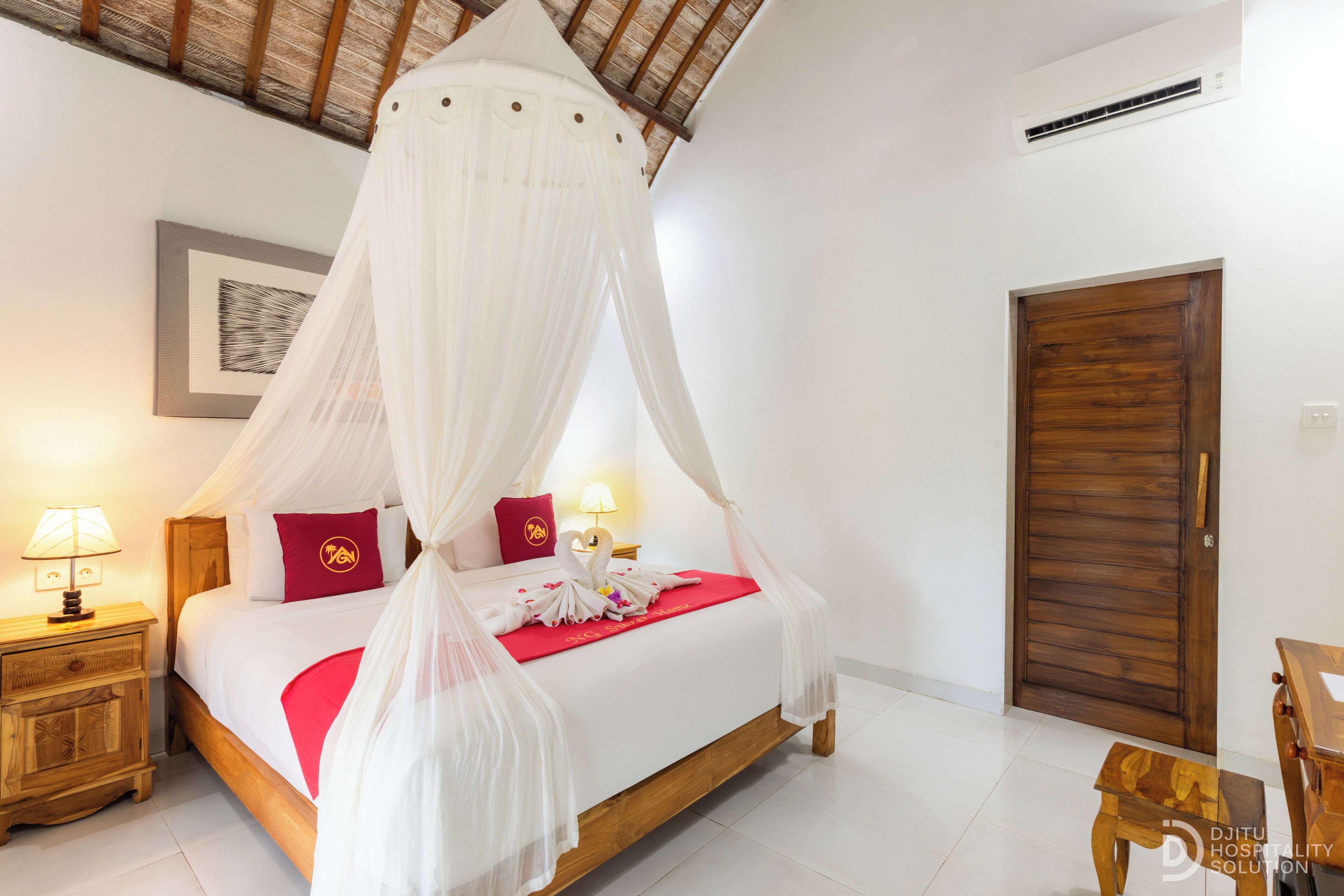 A bedroom with a four-poster canopy bed, wooden nightstands, a wooden door, and a framed picture on the wall.