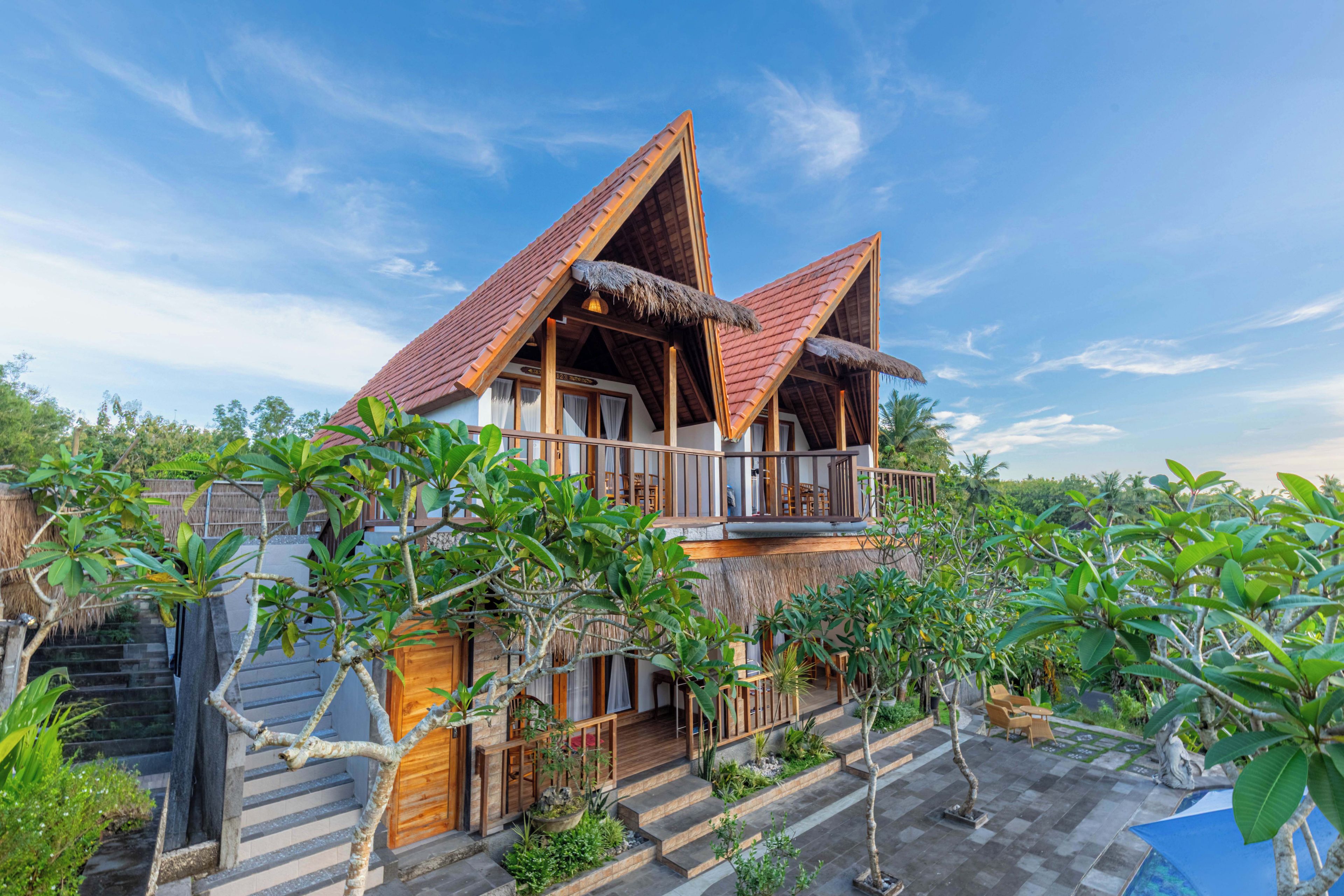 A two-story house with a thatched roof, wooden balconies, and a garden with tropical plants.
