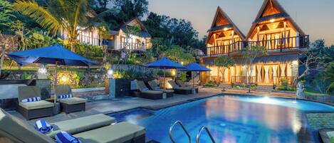 A resort with a swimming pool, lounge chairs, and thatched-roof buildings.