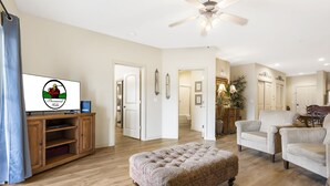 A spacious living room with a wooden floor, a tufted ottoman, and a ceiling fan. - Walk-In 2BR Branson Condo Near Strip | Sleeps 7 | Golf + Ticket Deals (Branson)