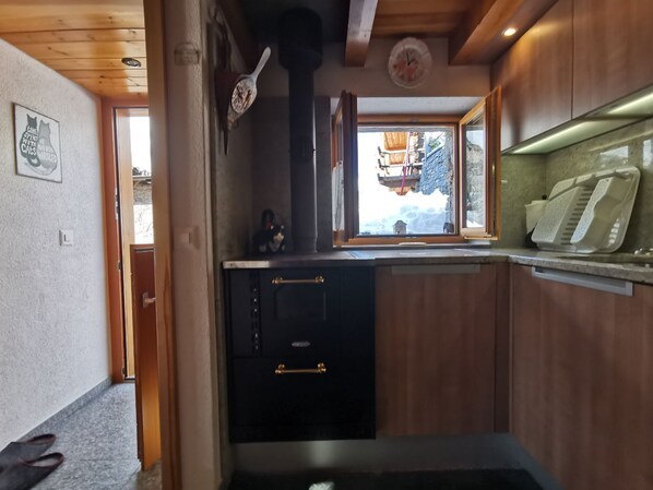 Cocina compacta con armarios de madera, un horno negro y una ventana con vistas al exterior.