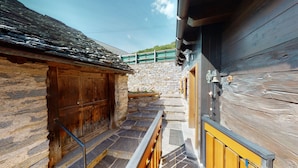 A narrow stone pathway leading to a wooden building with a stone wall and a wooden door. - Baita Dal Gat (Faido)