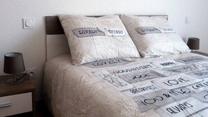 Una cama bien hecha con una colcha de edredón con texto estampado y dos almohadas con la inscripción 'LOVELY THINGS'.