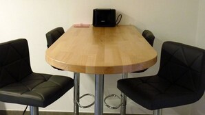 Una mesa de madera redonda con un altavoz negro encima, rodeada por cuatro sillas negras con patas de metal.