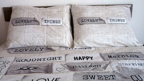 Una cama con almohadas y una colcha decorada con frases impresas como “lovely things”, “goodnight”, “happy”, “morning”, “daylight”, “love” y “sweet”. 