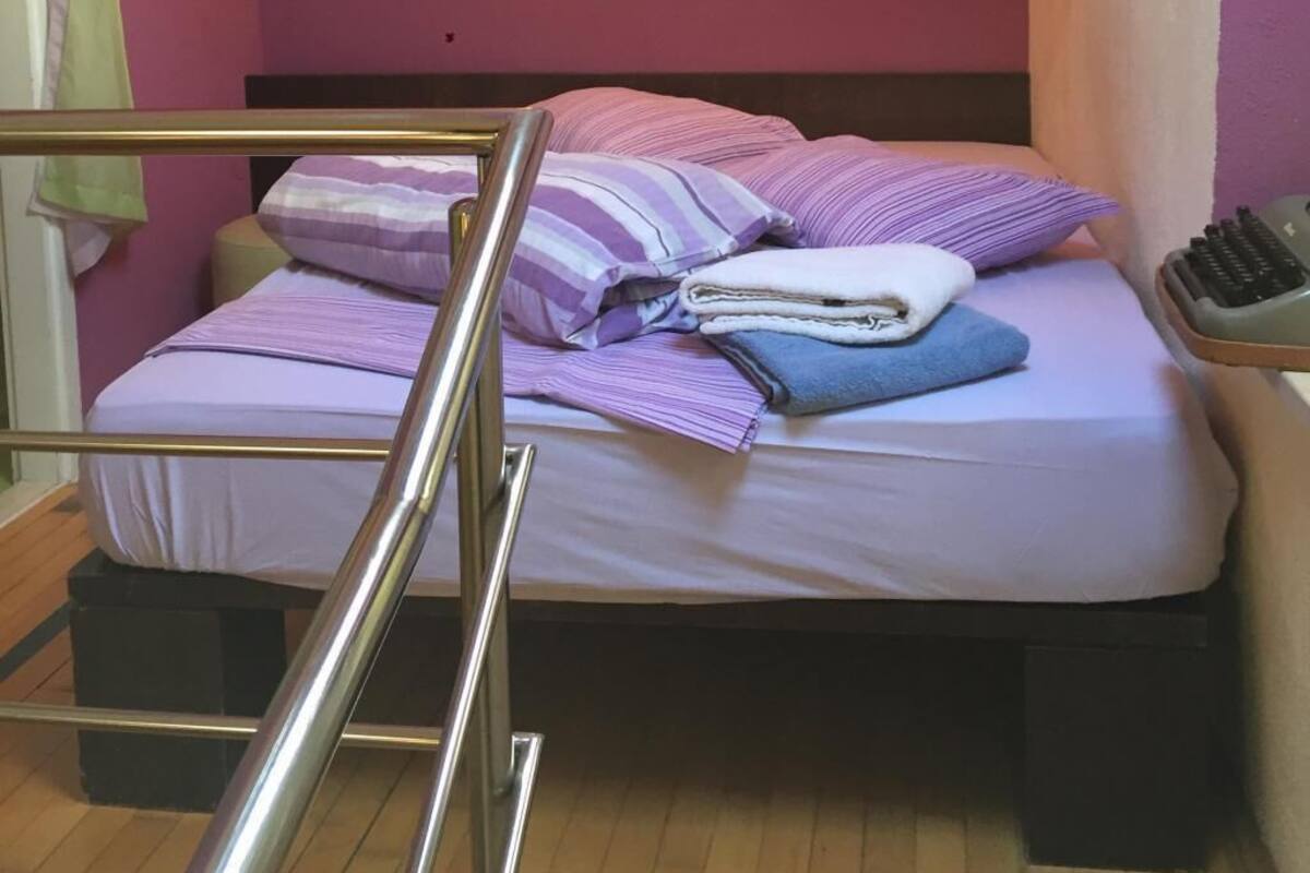 Un dormitorio pequeño y acogedor con cama, almohadas, una mesita de noche y un buró.