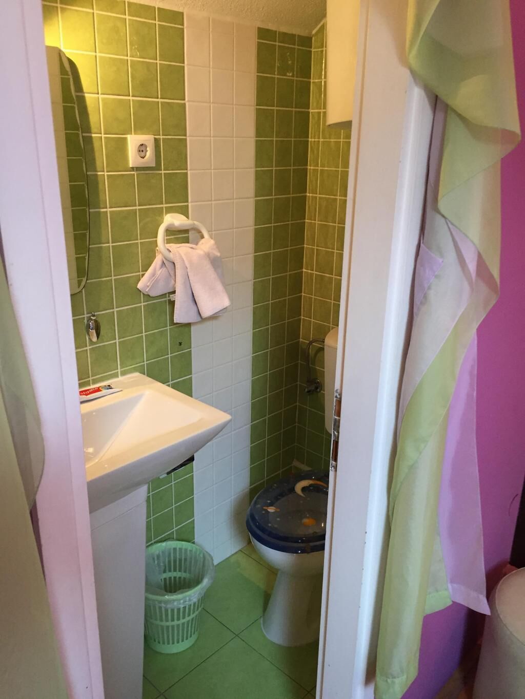 A small bathroom with green tiles, a white sink, a toilet, and a hanging towel.