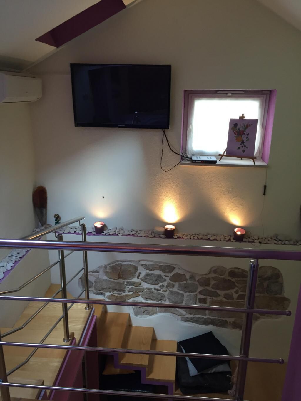 A staircase with a stone wall, a television mounted on the wall, and a small window with a painting.
