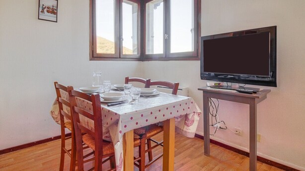 Un coin repas avec une table dressée pour quatre personnes, un téléviseur posé sur un meuble et une fenêtre donnant sur une colline.
